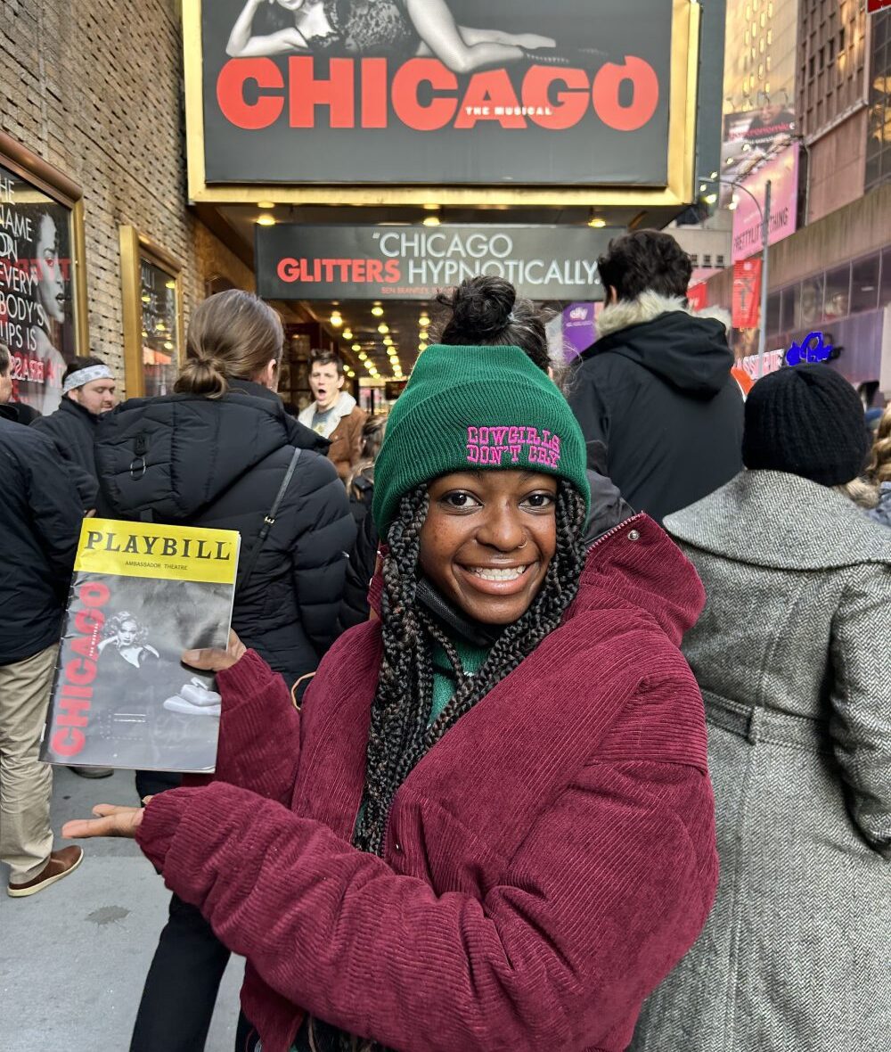 Person holding a "Chicago" Playbill outside a theater with a large "Chicago" billboard above.
