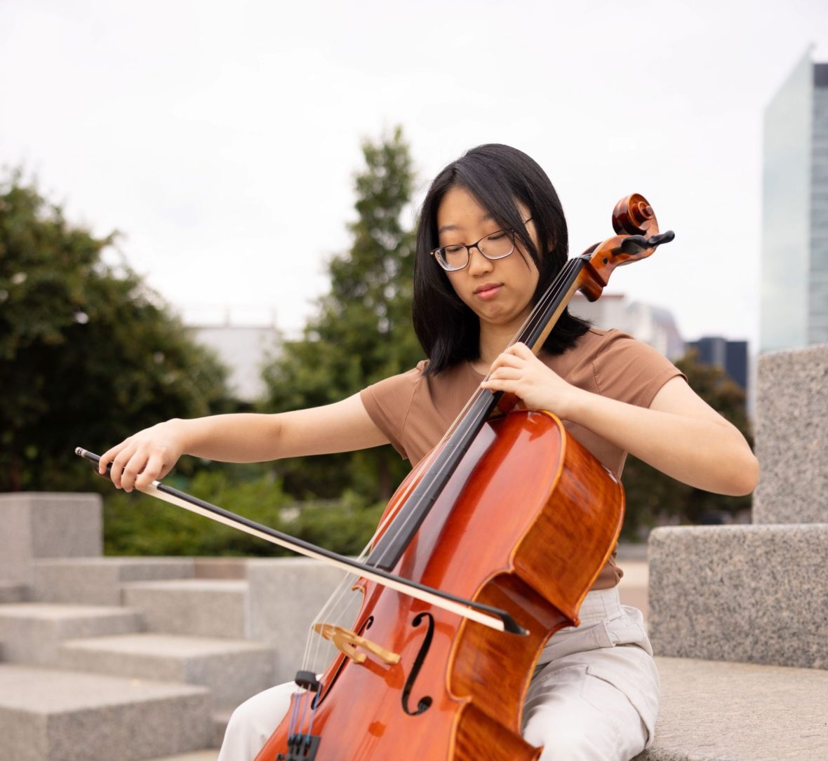A student playing the cello outside in the city