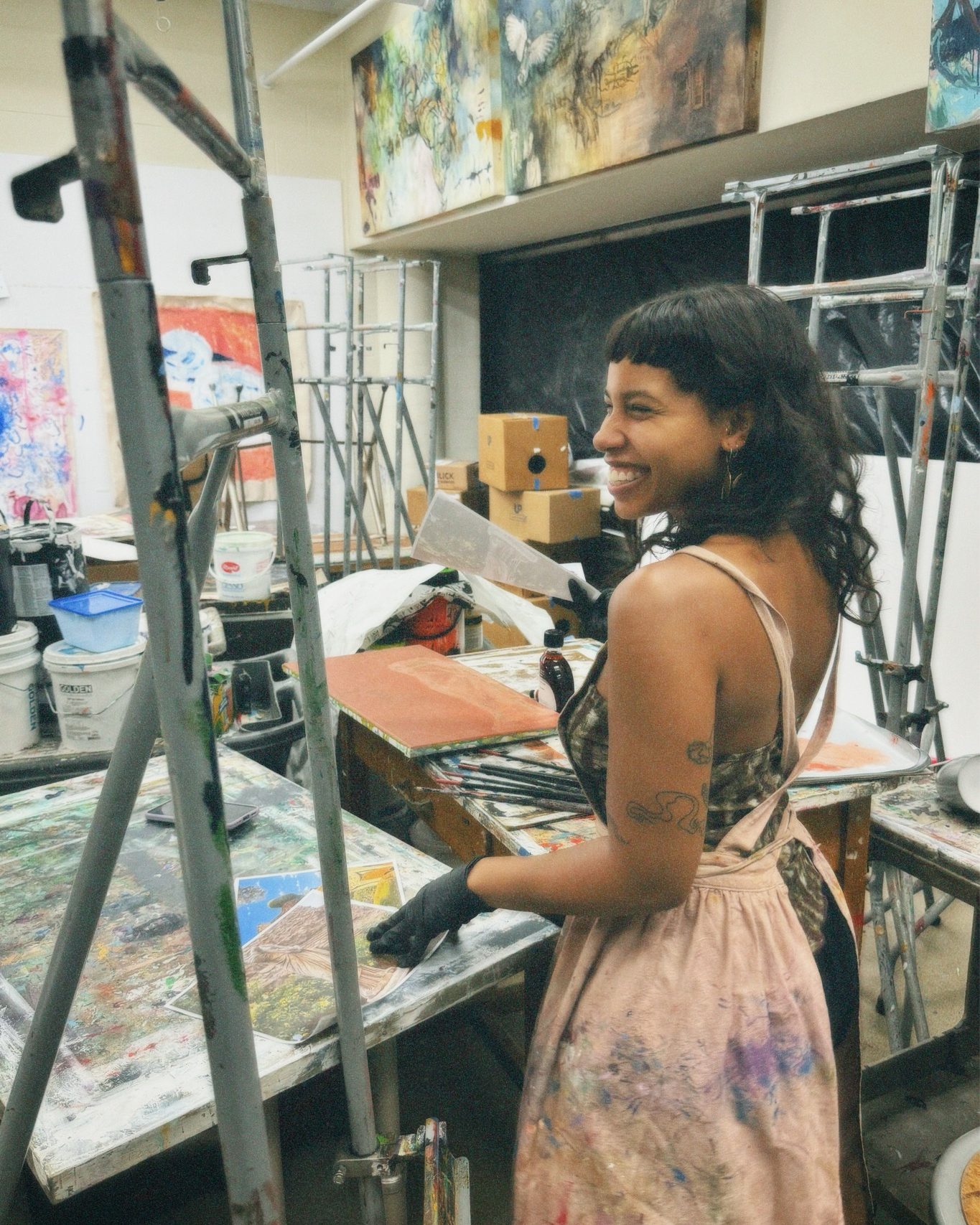 female art student in the painting studio smiling at an easel 
