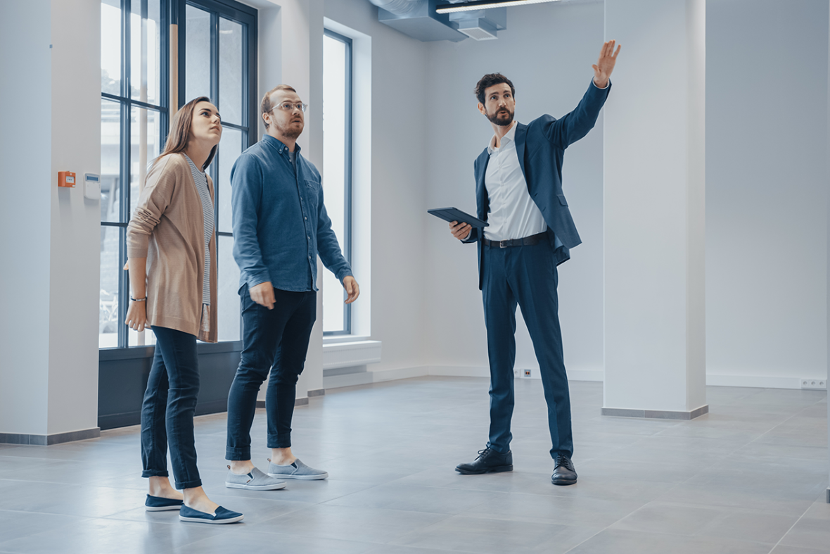 Real Estate Agent Showing a New Empty Office Space to Young Male and Female Hipsters. Entrepreneurs Meet the Broker with a Tablet and Discuss the Facility They Wish to Purchase or Rent.