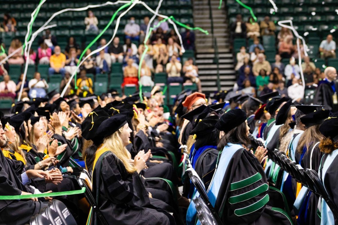 Commencement at UNC Charlotte with new graduates in seats and green and white confetti in the air.